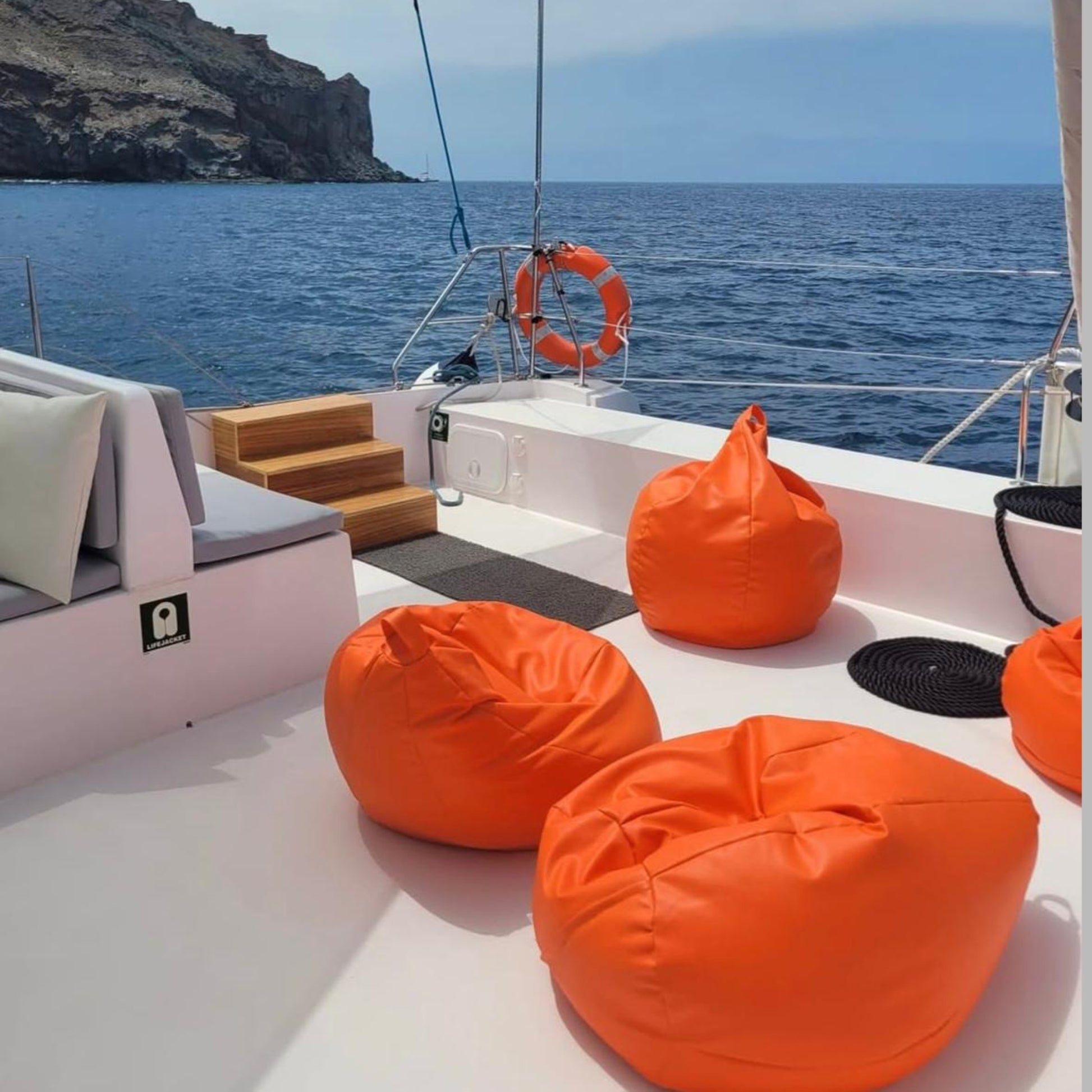 Orange bean bags on the stingray catamaran with ocean and cliff background