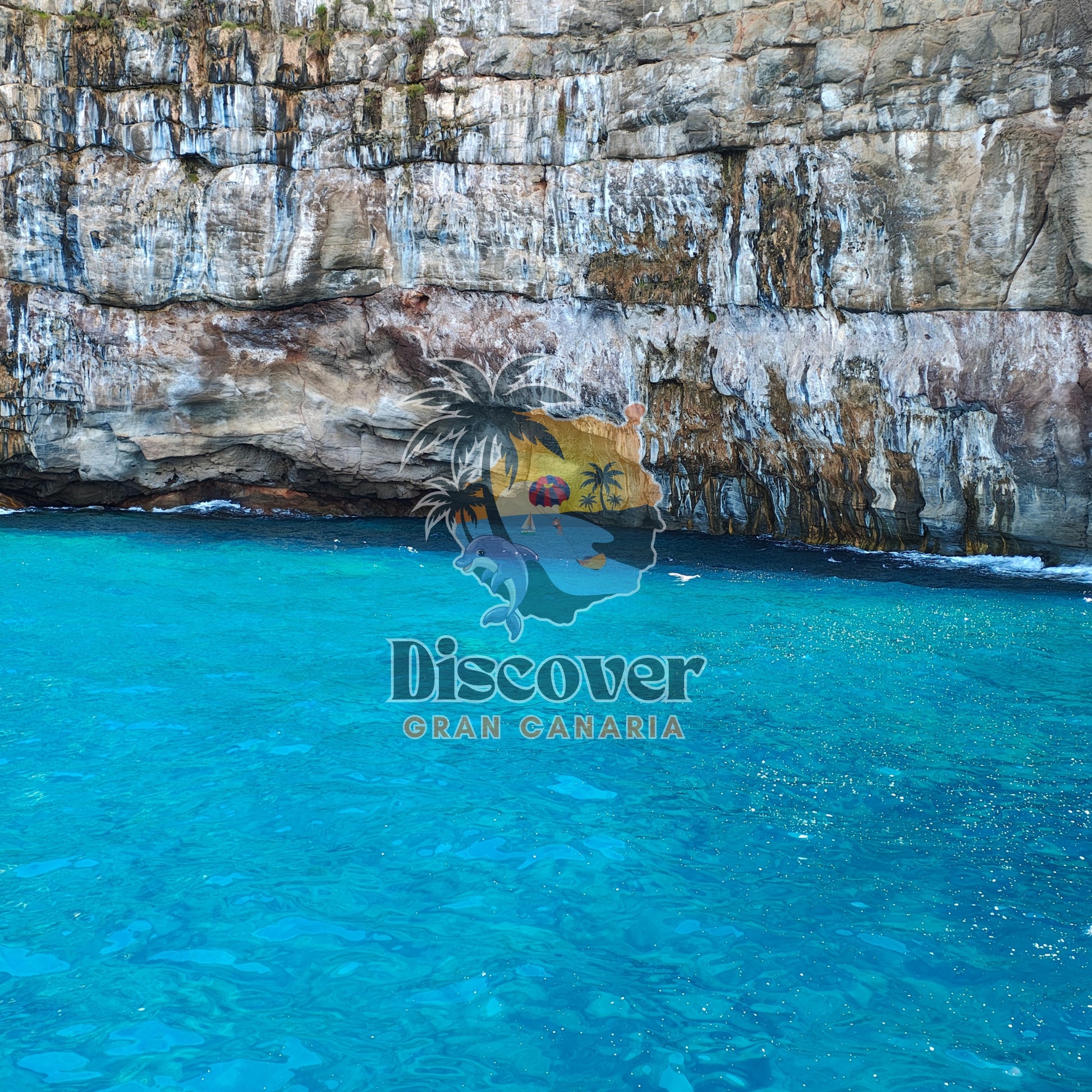 Cave entrance with turquoise water and rocky cliff face, featuring 'Discover Gran Canaria' logo.