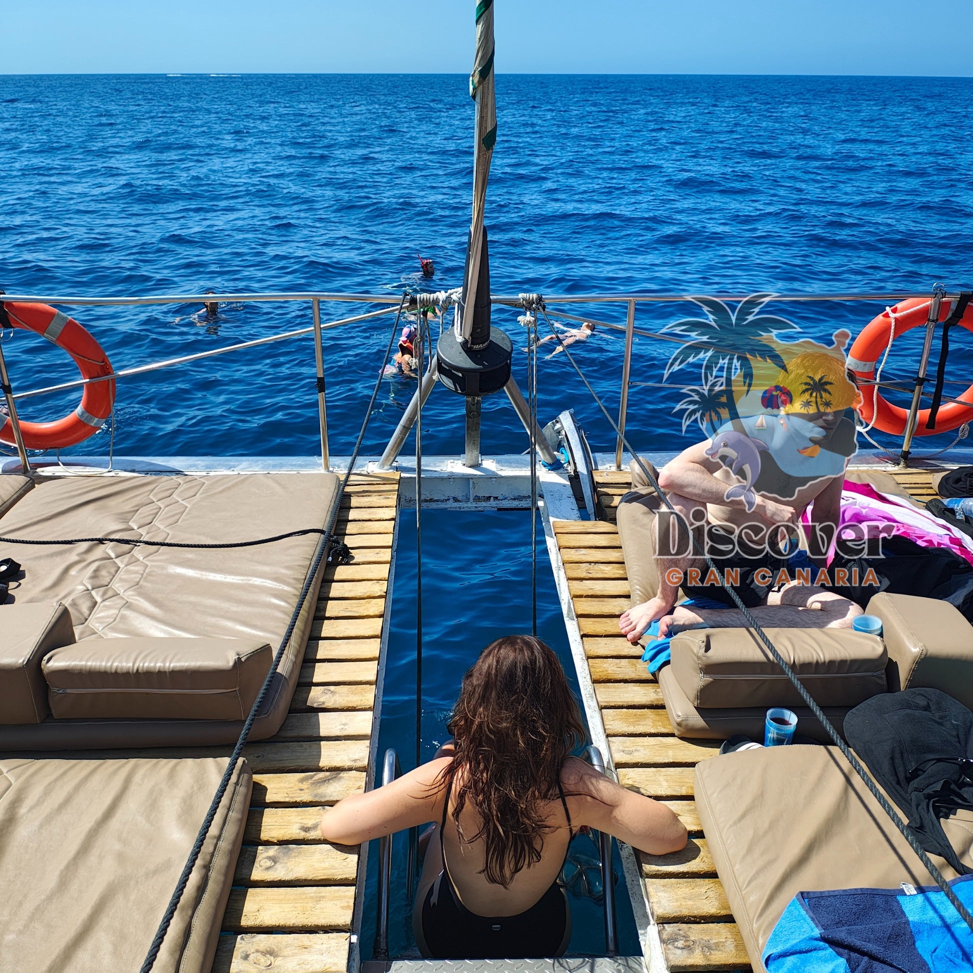 People on a boat with lounge chairs and a clear blue sea