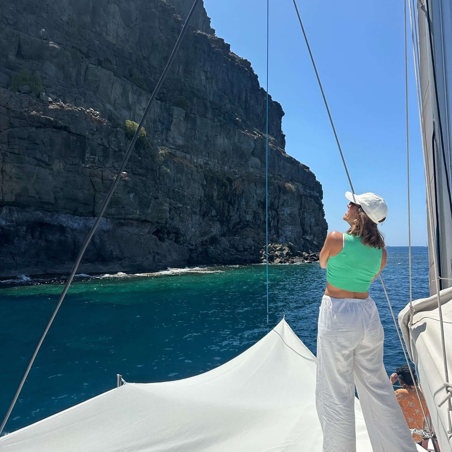 Woman on the stingray catamaran looking at a rocky cliff and blue sea