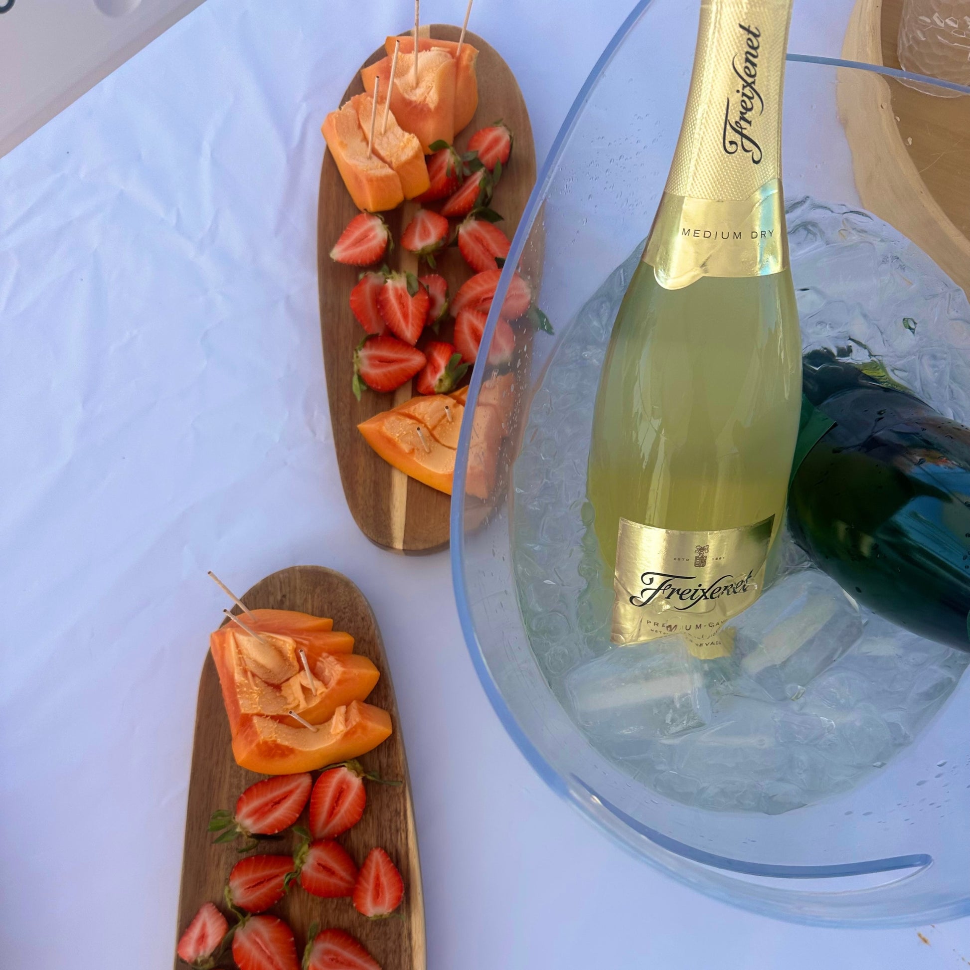 Bottle of Freixenet sparkling wine on ice with fruit skewers nearby.