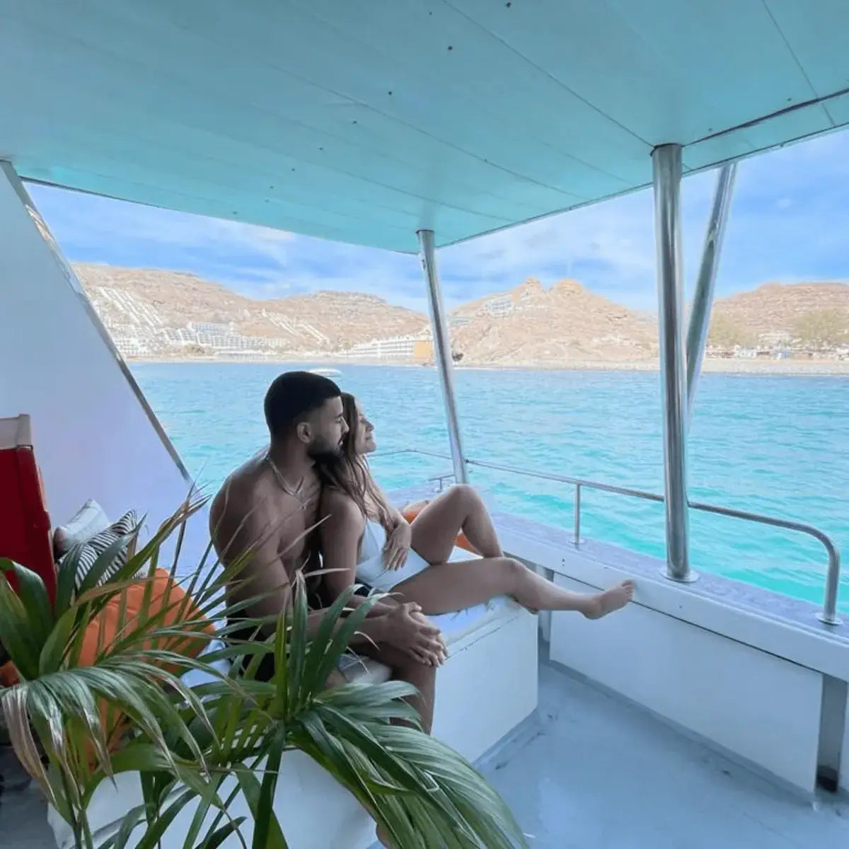 Two people sitting during the boat party grn canaria, looking out at a scenic view with mountains and clear blue water.