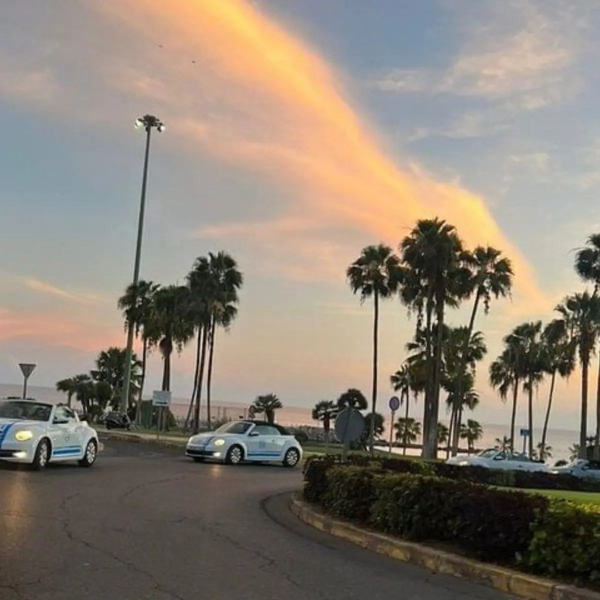 Two cars on a road with palm trees and a rainbow in the sky at Amadore Beach, Gran Canaria