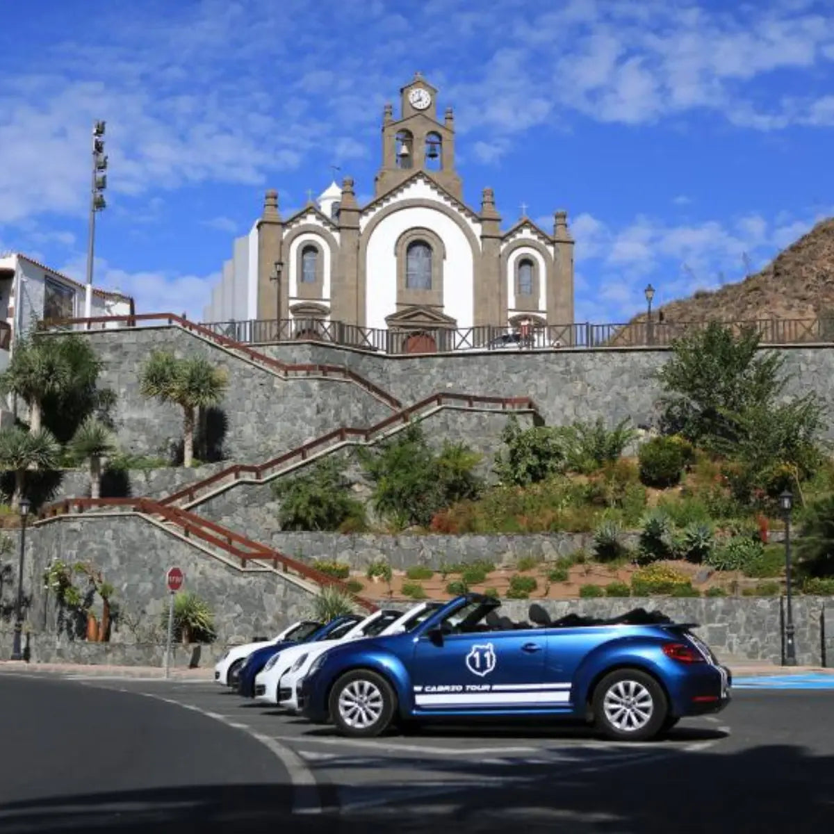 Blue convertible car with white stripes parked on a street in front of the church of Ingenio village in Gran Canaria.