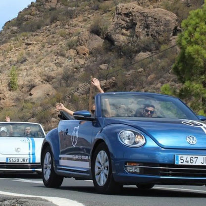 Blue Volkswagen Beetle convertible driving on a road with mountains in the background