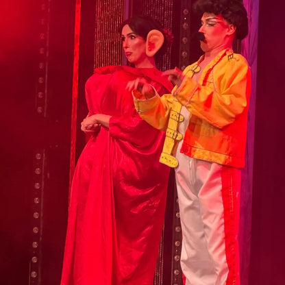 Two people in colorful costumes against a red background