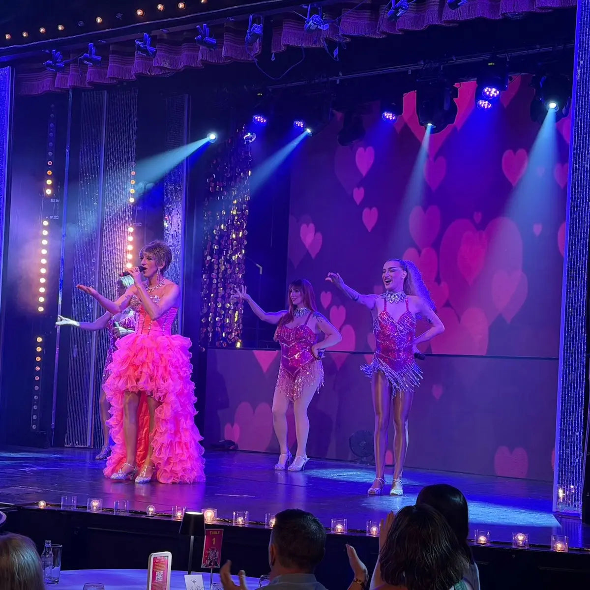 Three performers on a stage with a heart-patterned backdrop