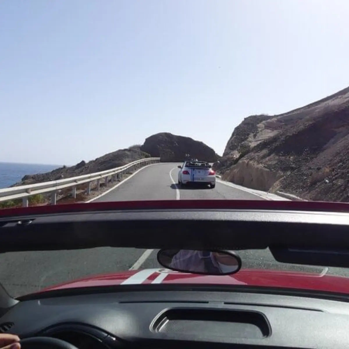 Car driving on a coastal road (GC500 Gran Canaria) with another car ahead, viewed from inside a vehicle.