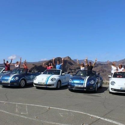 Group of people posing with convertible cars on a clear day at Degollada de la Yeguas in Gran Canaria