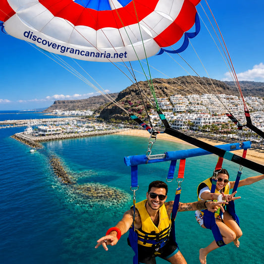 Two people parasailing over Puerto de Mogan Gran Canaria, with a colorful parasail.