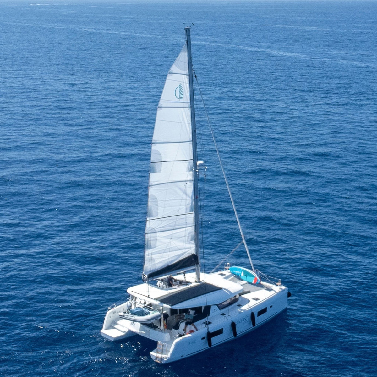 The bluefin catamaran on a vast blue ocean of Gran Canaria, captured from an aerial perspective with its main sail fully deployed.
