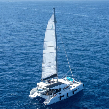 The bluefin catamaran on a vast blue ocean of Gran Canaria, captured from an aerial perspective with its main sail fully deployed.